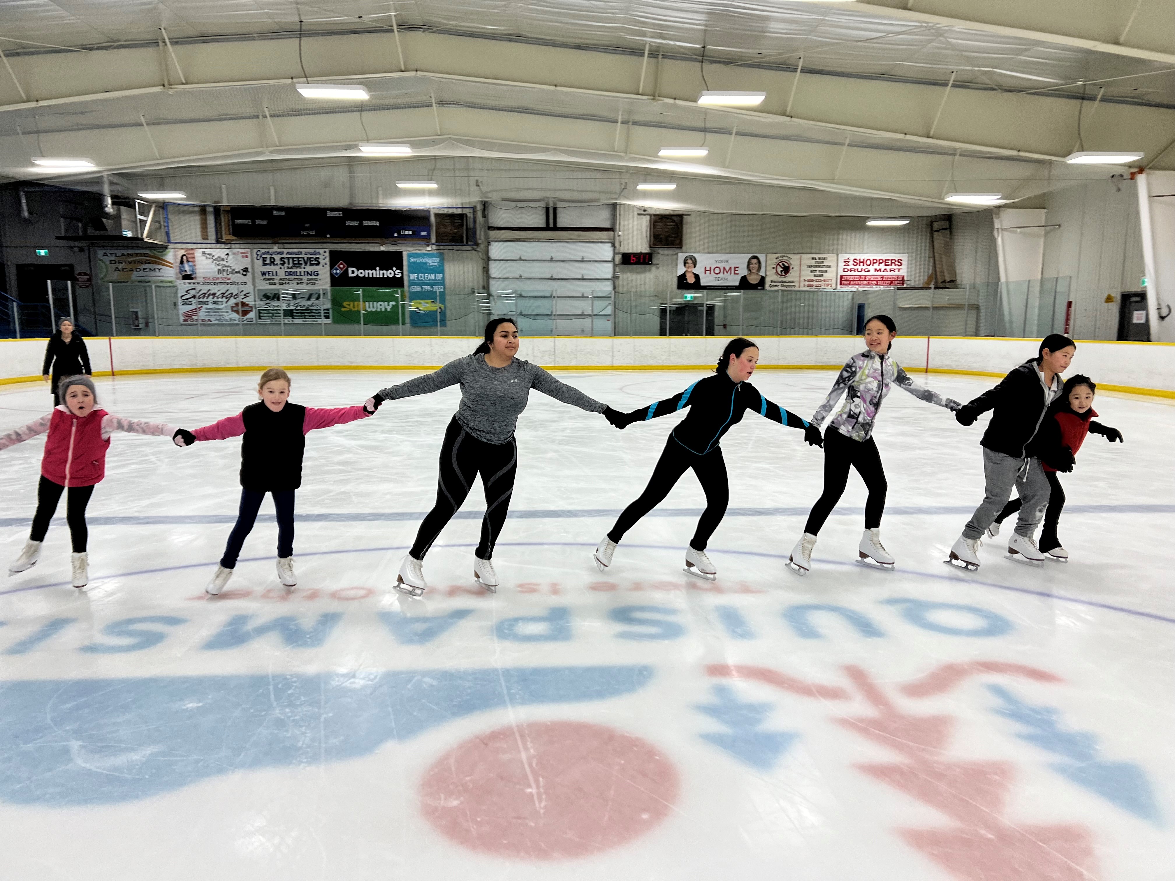 Group of young figure skaters holding hands skating.